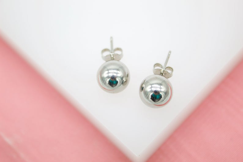 A pair of shiny silver ball stud earrings rests on a white display surface.