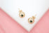 A pair of polished gold ball stud earrings rests elegantly on a white surface against a soft pink background.