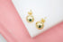 Two polished gold ball stud earrings rest on a white surface with a pink background.