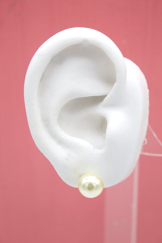 A white mannequin ear displays a lustrous cream-colored pearl stud earring against a pink background.