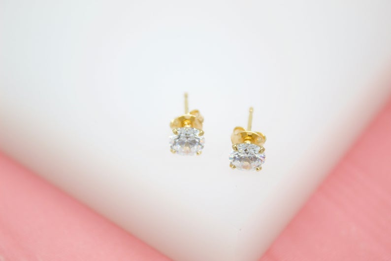 A pair of gold stud earrings featuring sparkling cubic zirconia stones rests neatly on a white surface.