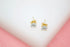 A pair of gold stud earrings featuring sparkling cubic zirconia stones rests neatly on a white surface.