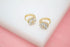 Two gold hoop earrings featuring sparkling flower-shaped zirconia crystal charms rest on a white surface.