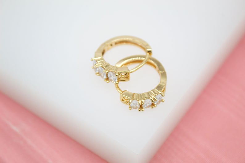 Two shimmering gold hoop earrings featuring embedded sparkling cubic zirconia stones rest on a white surface.