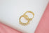 Two gold huggie hoop earrings featuring sparkling clear cubic zirconia stones rest on a white surface with a pink background.
