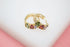 A pair of gold huggie hoop earrings features colorful multi-gemstones resting on a clean white and pink surface.
