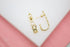 A pair of gold huggie hoop earrings featuring an interconnected heart pattern rests against a white and pink background.