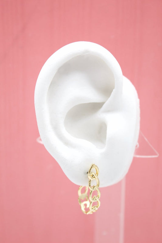 A white mannequin ear displays a gold chain-link hoop earring against a pink background.