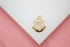 A gold medallion pendant features a pavé-set diamond heart on a white surface with a pink background.