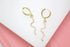 A pair of gold snake hoop earrings with pavé crystals and green eyes rests on a white surface.