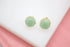 A pair of round green jade gemstone stud earrings in gold settings rests on a white display surface.