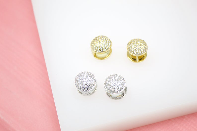 Four sparkling pave dome huggie earrings in gold and silver rest neatly on a white display against a soft pink background.