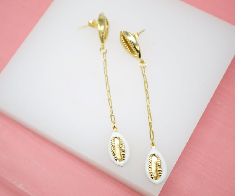 A pair of elegant gold chain drop earrings features white and gold cowrie shells on a white display block.
