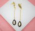 A pair of gold dangle earrings features cowrie shell studs connected by delicate chains to black and gold cowrie shell pendants.