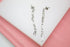 A pair of silver paperclip chain drop earrings rests against a white and pink display surface.