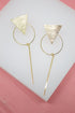 A pair of gold geometric drop earrings featuring a textured triangle, circle, and vertical bar display against a white and pink background.