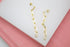 A pair of elegant gold chain link drop earrings rests against a white and pink display surface.