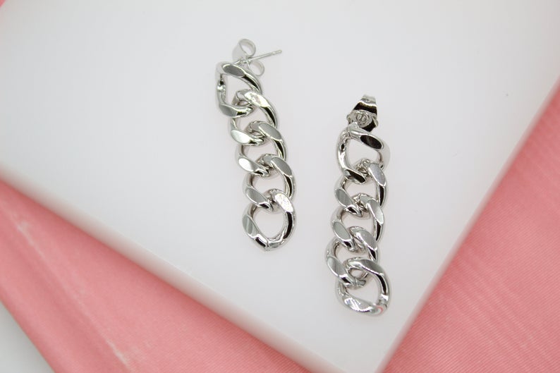A pair of silver chain link drop earrings rests on a white display surface against a soft pink background.
