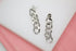 A pair of silver chain link drop earrings rests on a white display surface against a soft pink background.