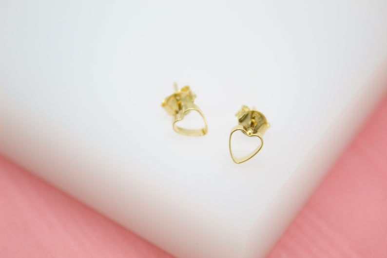 A pair of delicate gold heart-shaped stud earrings rests on a white display surface.