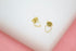 A pair of delicate gold heart-shaped stud earrings rests on a white display surface.