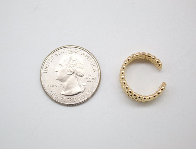 A textured gold ear cuff rests beside a US quarter coin for size comparison.