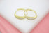 A pair of gold huggie hoop earrings embedded with small white baguette crystals rests on a white and pink surface.