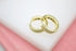 A pair of sparkling gold huggie hoop earrings with pave diamonds rests on a white and pink display.