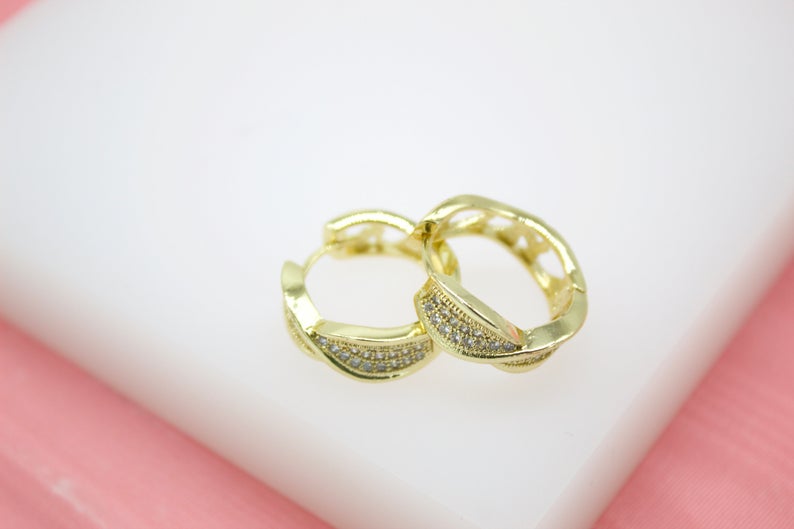 A pair of gold hoop earrings with sparkling pave-set cubic zirconia stones rests elegantly on a white surface.