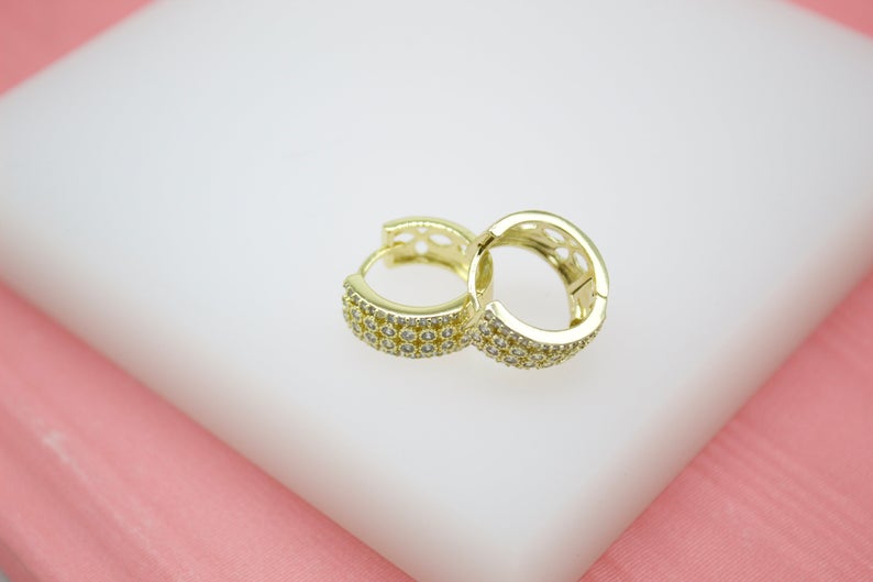 A pair of glittering gold hoop earrings rests gracefully on a white display surface against a soft pink backdrop.