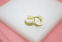 A pair of glittering gold hoop earrings rests gracefully on a white display surface against a soft pink backdrop.