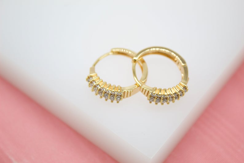 Two small gold hoop earrings feature rows of sparkling clear cubic zirconia stones.