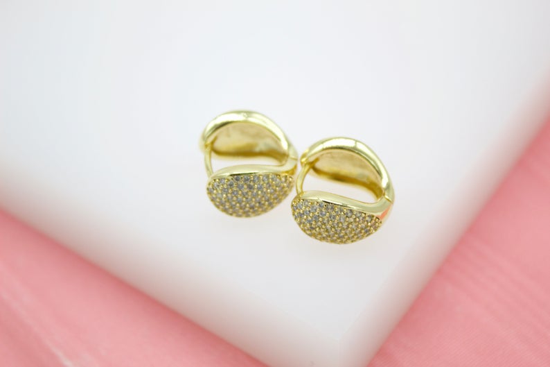 A pair of gold huggie hoop earrings featuring sparkling pavé-set cz stones rests on a white surface.