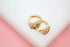 A pair of gold huggie hoop earrings featuring sparkling multicolored cubic zirconia stones rests on a white and pink surface.
