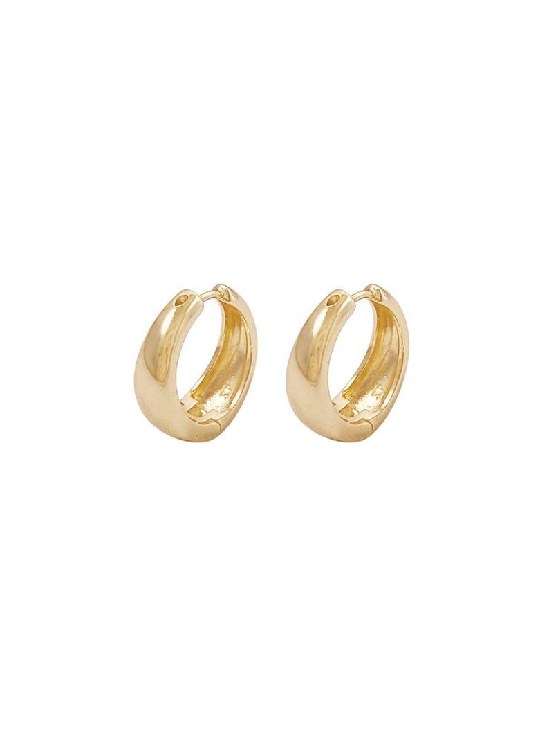 A pair of shiny gold huggie hoop earrings rests against a clean white background.