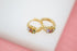 A pair of gold huggie hoop earrings featuring colorful cubic zirconia stones rests on a white and pink surface.
