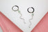 A pair of silver snake hoop earrings features sparkling cubic zirconia bodies and striking green crystal eyes against a white and pink background.