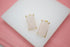 A pair of rectangular rose quartz gemstone earrings in gold settings rests on a white display surface.