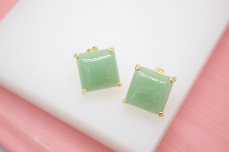 Two square green gemstone stud earrings rest neatly on a clean white surface.