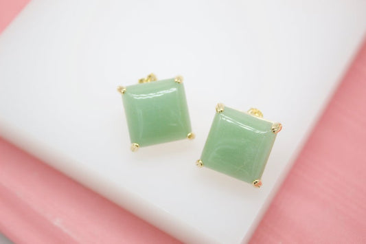 Two square green gemstone stud earrings rest neatly on a clean white surface.