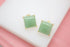 Two square green gemstone stud earrings rest neatly on a clean white surface.