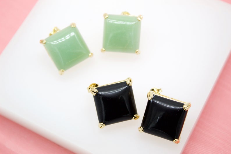 Two pairs of square stud earrings featuring green jade and black onyx stones set in gold rest on a white surface.