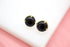 Two round black gemstone stud earrings featuring secure gold prong settings rest on a white display surface.