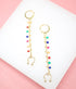 A pair of gold dangle earrings featuring long chains adorned with colorful enamel beads rests on a white display surface.