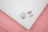 A pair of sparkling silver-toned cuff links with crystal-encrusted domes rest on a clean white display surface against a soft pink background.