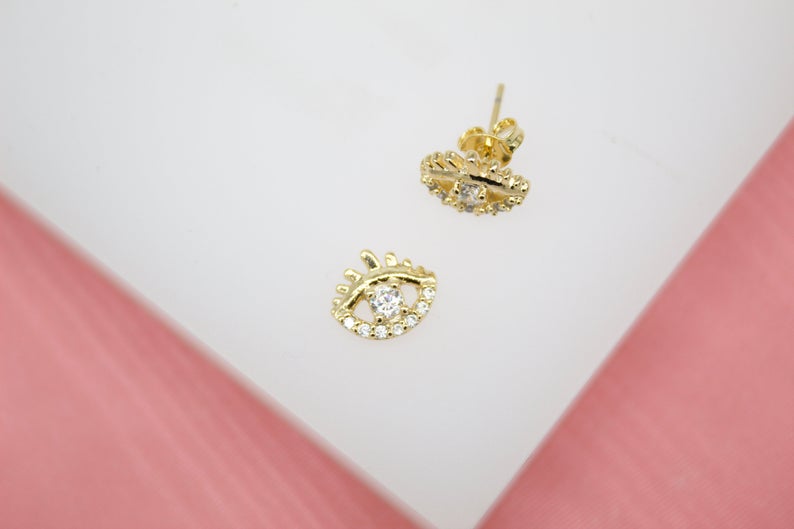 A pair of gold evil eye stud earrings features sparkling cubic zirconia stones nestled inside the eye design.