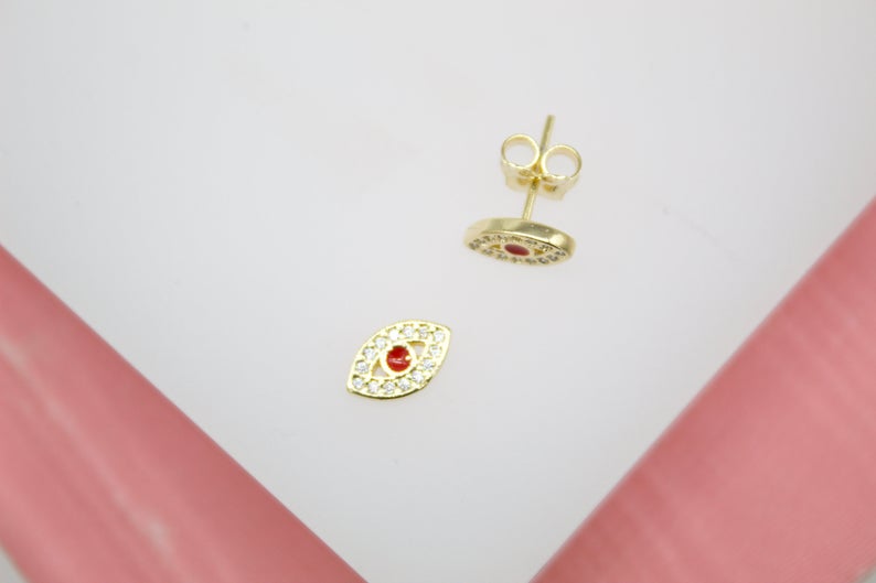 A pair of gold evil eye stud earrings features sparkling cubic zirconia and a bright red center stone.