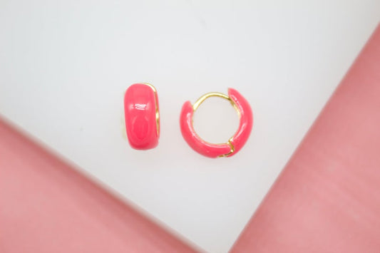A pair of vibrant neon pink enamel hoop earrings rest on a white surface.