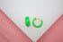 A pair of vibrant neon green enamel hoop earrings rests on a white display surface.
