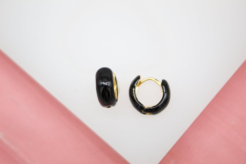 A pair of glossy black enamel hoop earrings rests against a white and pink surface.